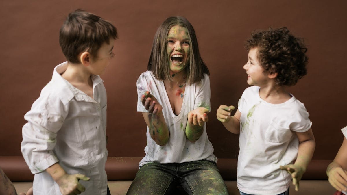 Smiling children and woman enjoy vibrant holi festival with colorful powder indoors.